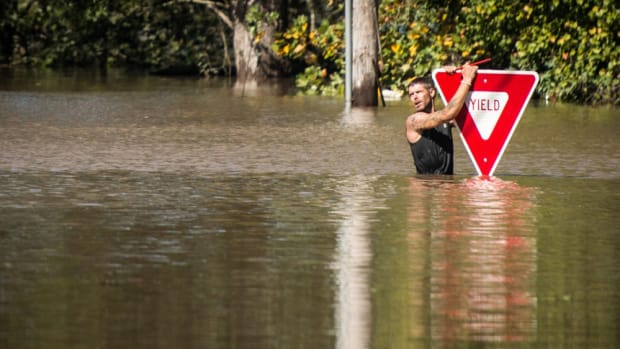 A man is shown holding on to a yield sign after trying to swim out to help a stranded truck driver at U.S. 301 and Tom Starling Road in Hope Mills, N.C., on Sunday. Both people were rescued. Fayetteville Observer photo by Andrew Craft.